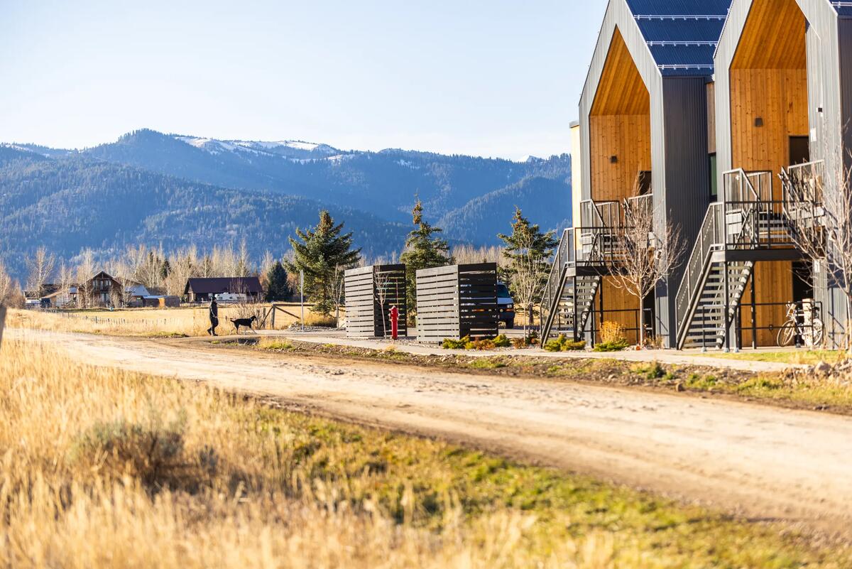 Resident walking a dog past Teton Flats entries with the snow-dusted Teton Range in the distance