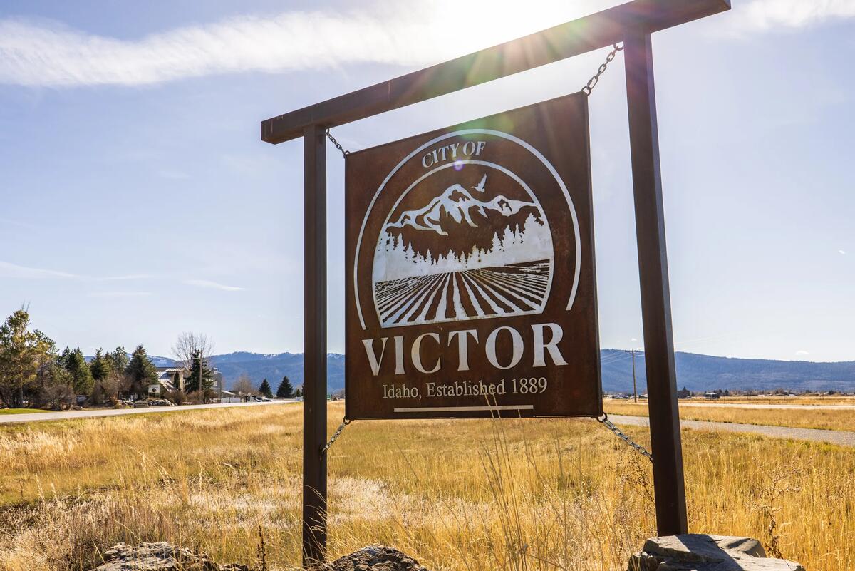 City of Victor, Idaho welcome sign, established 1889, in tall golden grass with mountains behind